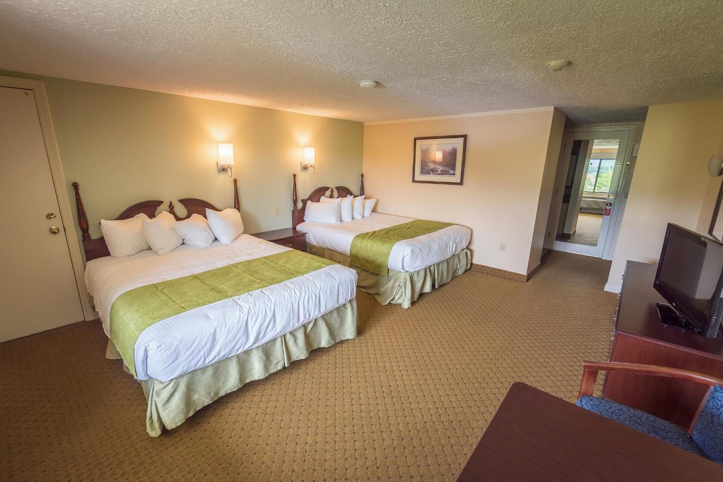 A hotel room with two beds, a TV, and a desk.
