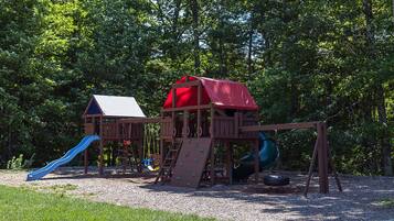 Children can play in the playground with a playhouse, slide, and spiral slide set amidst lush greenery.