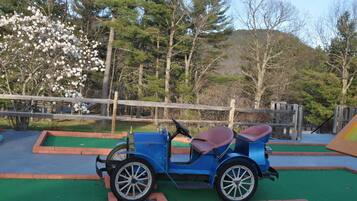 Ein blauer Oldtimer mit rotem Sitz auf einer Grünfläche, im Hintergrund ein Holzzaun.