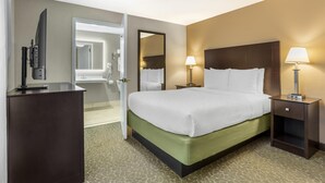 A hotel room with a bed, bedside lamps, a TV, and a bathroom visible through an open door.