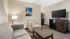A hotel room with a sofa, armchair, coffee table, TV, and a painting on the wall.