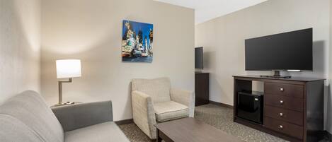 A hotel room with a sofa, armchair, coffee table, TV, and a painting on the wall.