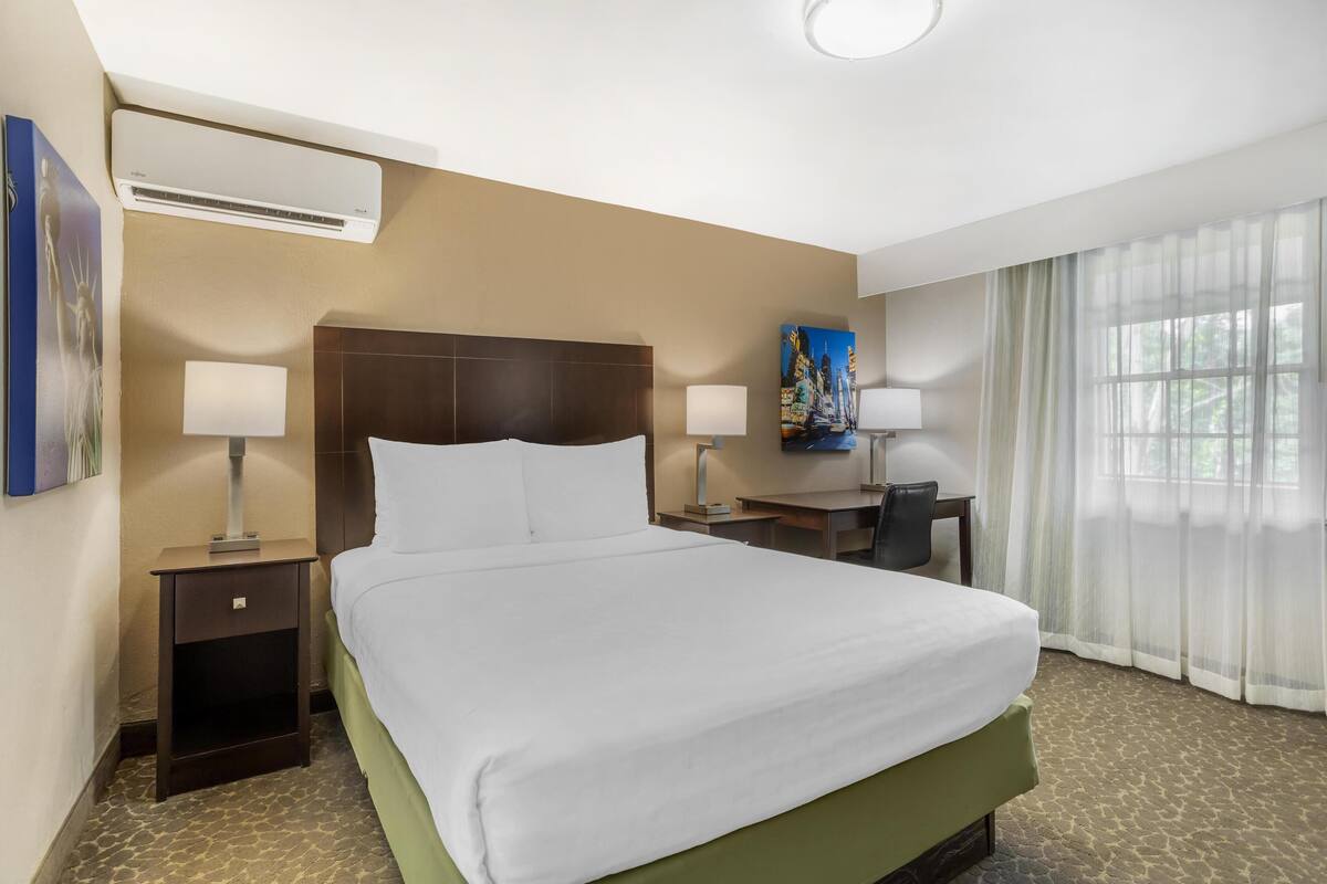 A hotel room with a large bed, two bedside tables with lamps, a desk, and a chair.