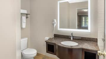A bathroom with a white toilet, a sink with a granite countertop, a hairdryer, and a mirror.