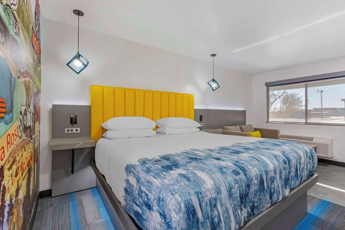 A modern hotel room with a large bed, a yellow headboard, and a large window.