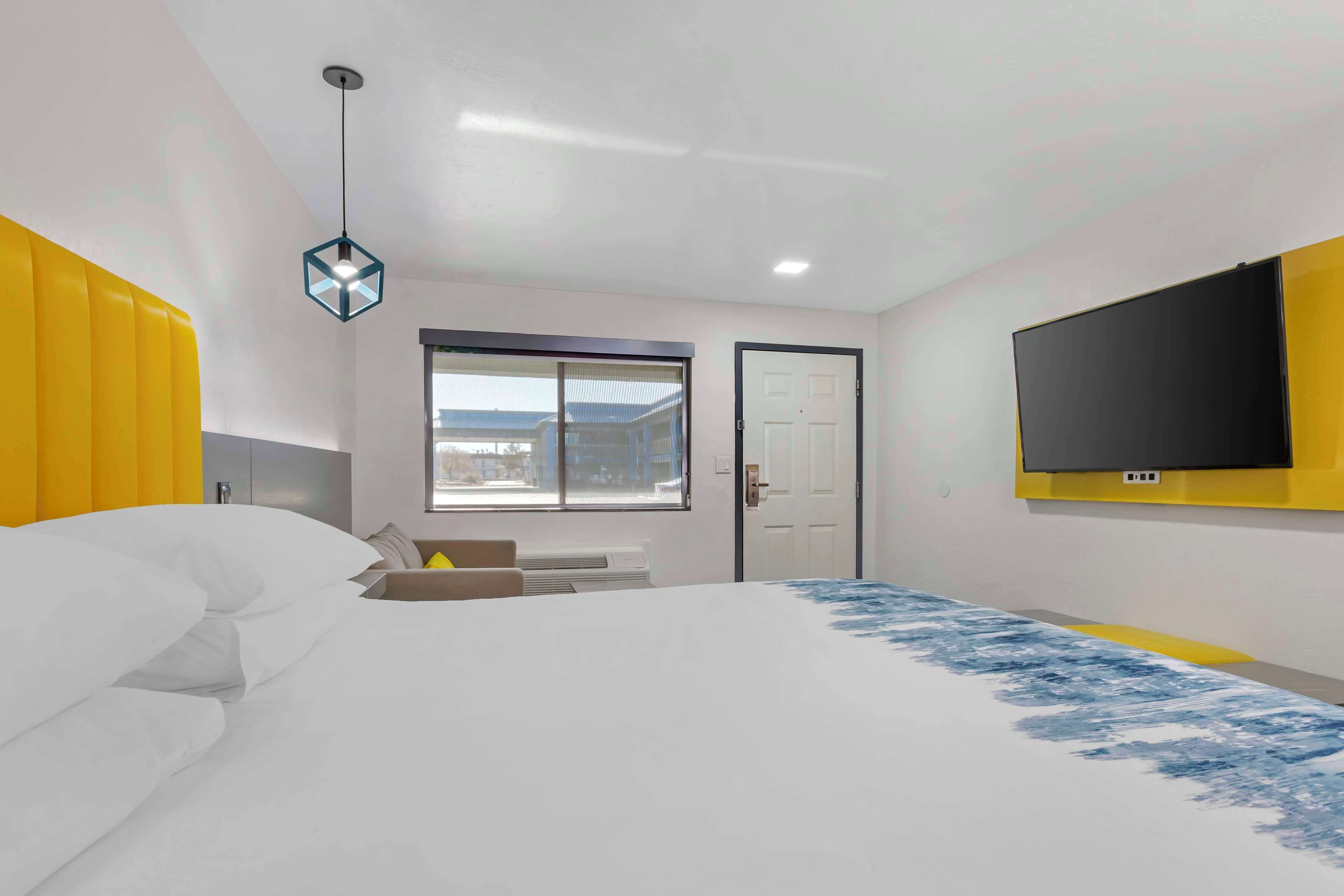 A bedroom with a large bed, a TV mounted on the wall, and a window with a view of buildings.