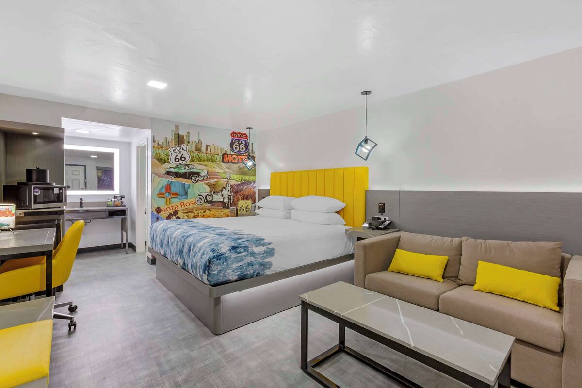 A hotel room with a bed, a sofa, a desk, and a kitchenette.