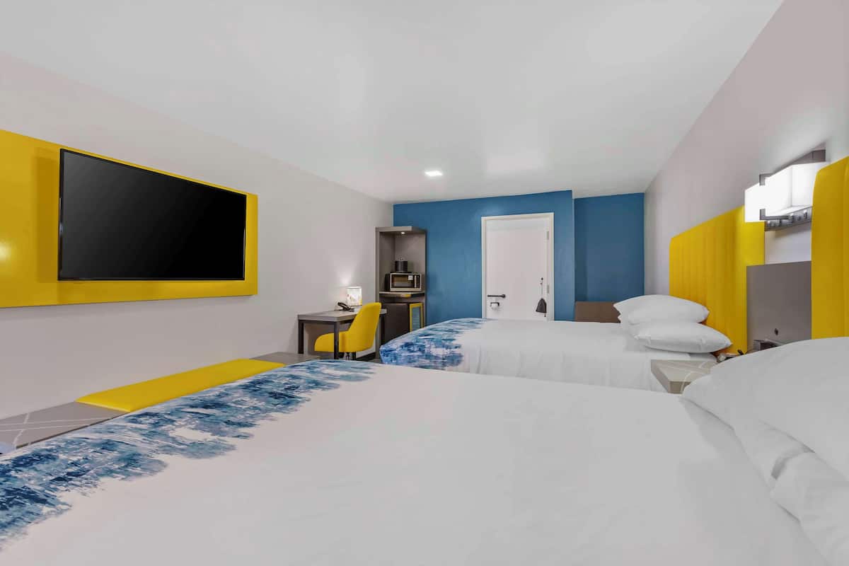 A hotel room with two beds, a desk, a chair, and a TV mounted on the wall.