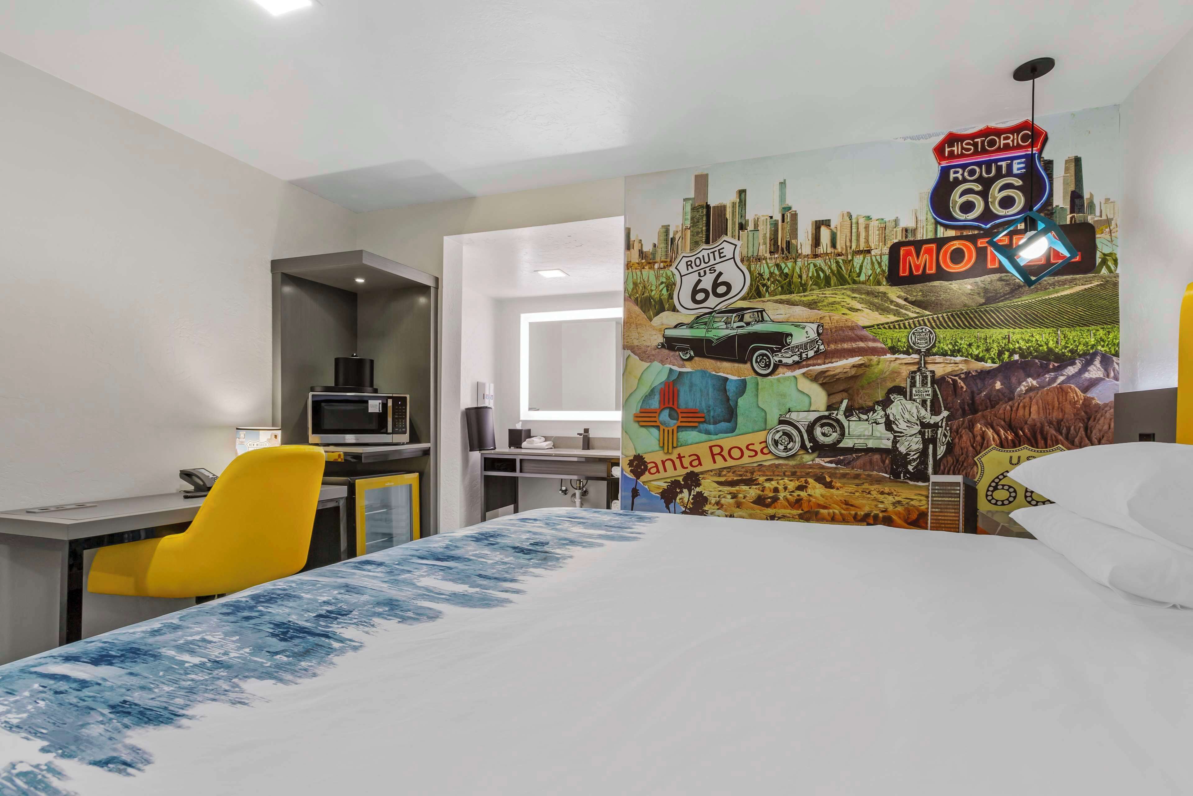 Una habitación de hotel con cama, escritorio, silla y un mural que representa la Ruta 66.