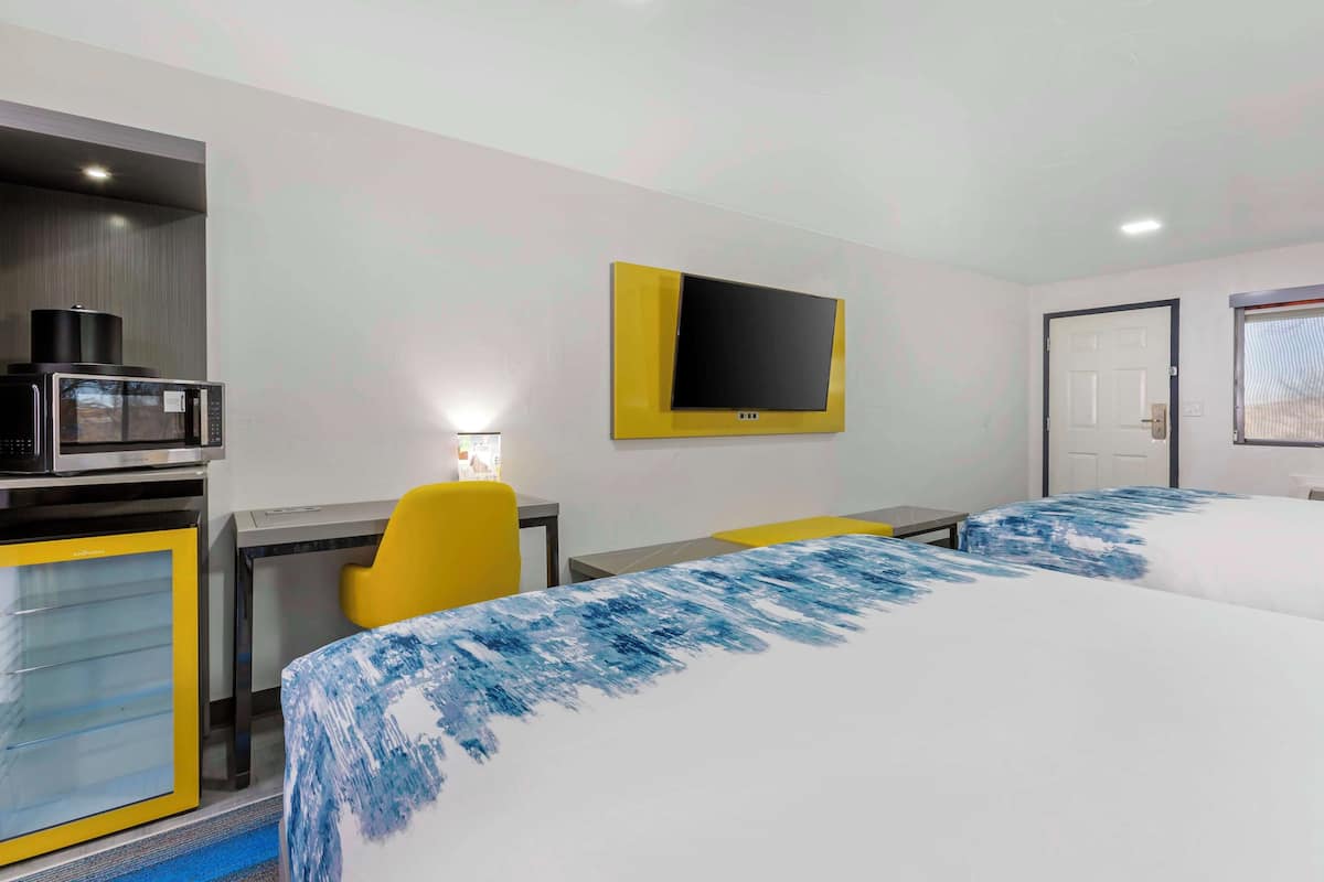 A hotel room with a bed, a desk, a chair, a television, and a microwave.