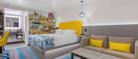 A modern hotel room with a bed, a sofa, a desk, and a wall mural.
