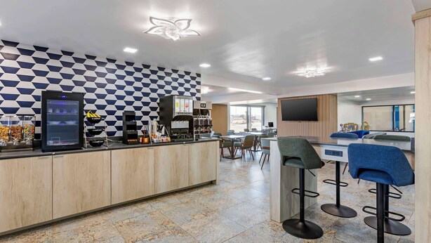 A modern bar area with a checkered wall pattern, a digital screen, and a counter with various items. There are bar stools and a seating area with tables. - Hotel Blue 66, BW Signature Collection (Santa Rosa)