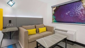A modern hotel room with a sofa, a small table, a desk with a lamp, a large painting, and a wall-mounted air conditioner. - Hotel Blue 66, BW Signature Collection (Santa Rosa)