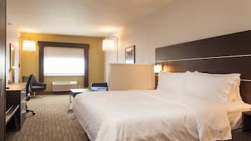 A hotel room with a large bed, a desk, a chair, a lamp, and a window.