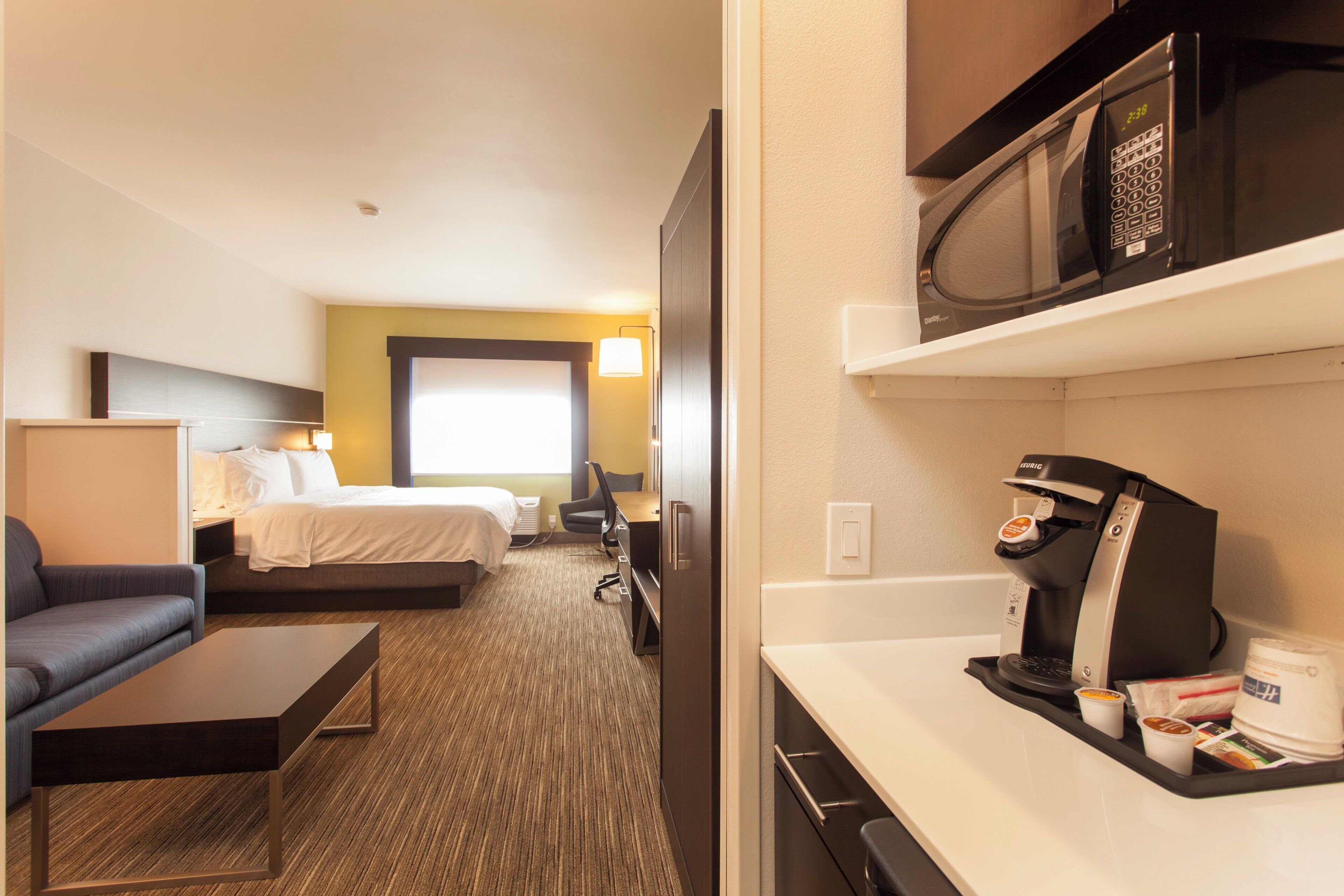 Habitación de hotel con cama, escritorio, silla, microondas y cafetera.
