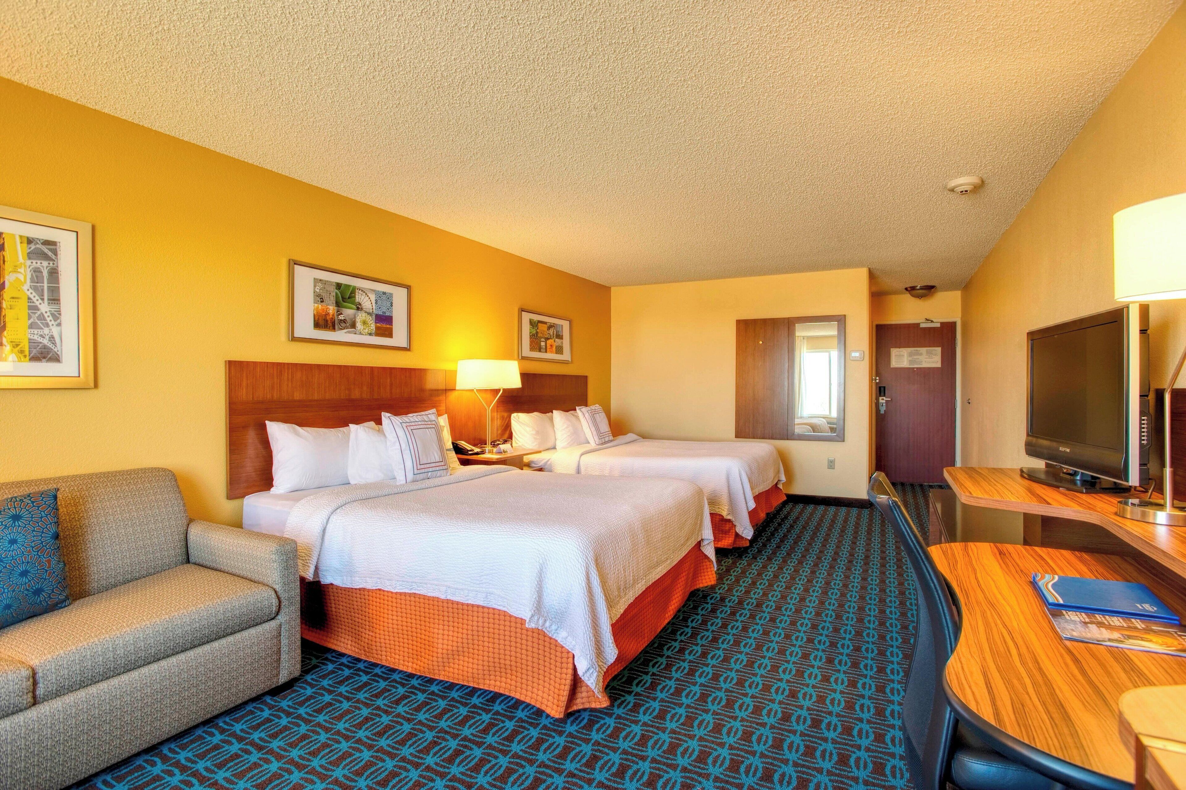 A hotel room with two beds, a sofa, a desk, a TV, and a patterned carpet.