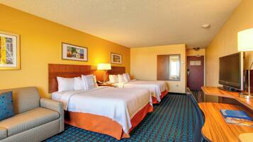 A hotel room with two beds, a sofa, a desk, a TV, and a patterned carpet.