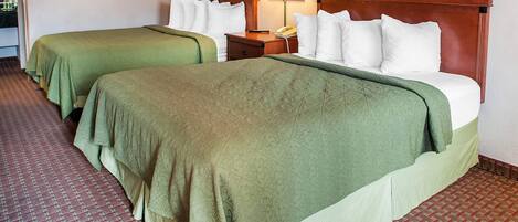 A hotel room with two beds, each with green bedding, a wooden headboard, a nightstand with a lamp, and a telephone.