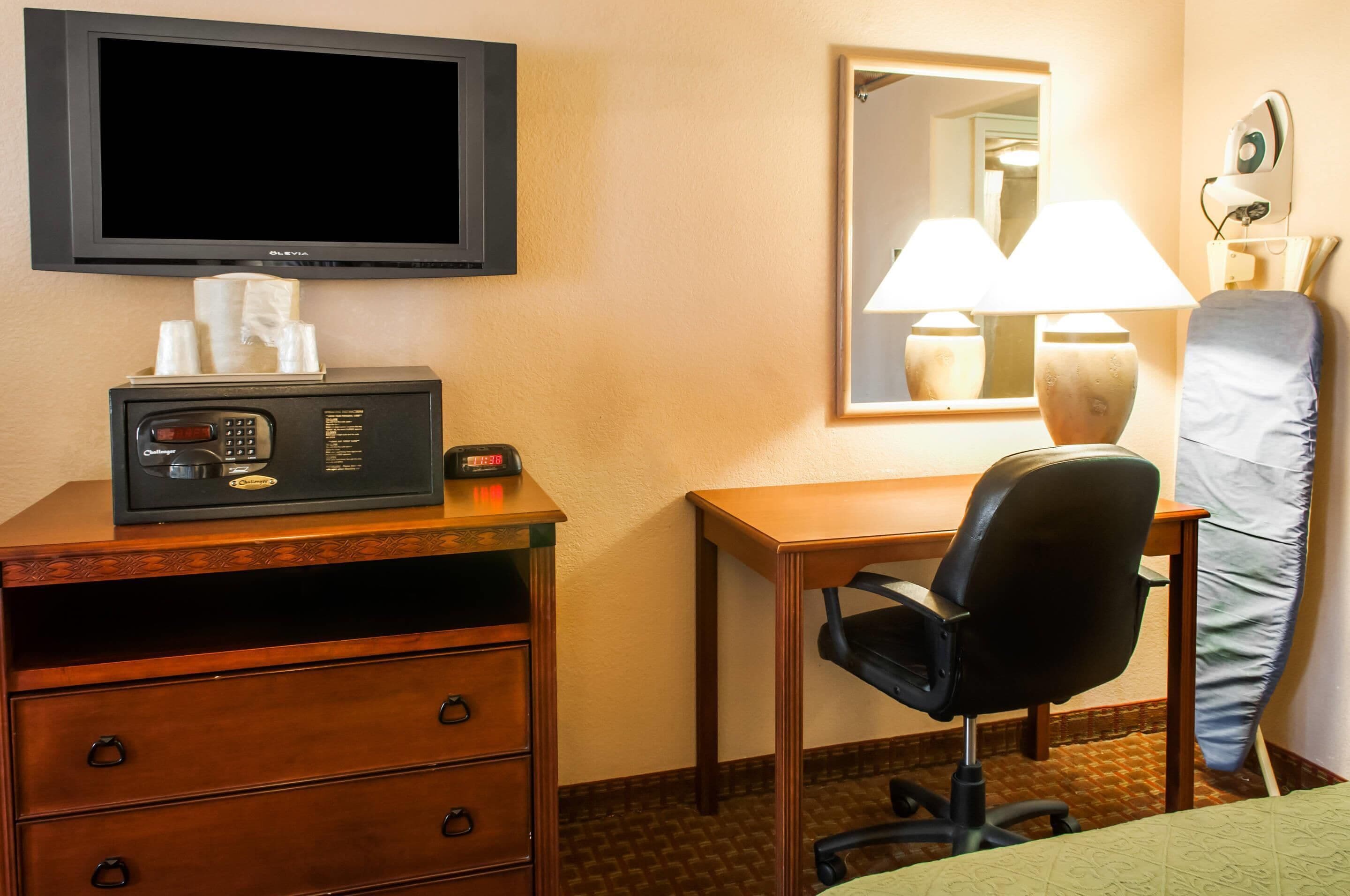 Ein Hotelzimmer mit Schreibtisch, Stuhl, Fernseher, Nachttisch mit Lampe und Bett.