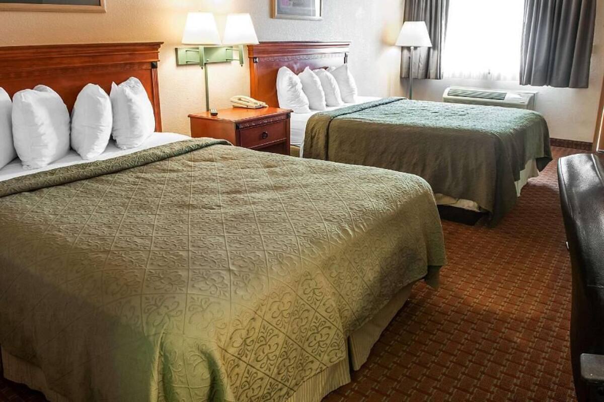 Ein Hotelzimmer mit zwei Betten, einem Nachttisch, einer Lampe, einem Telefon und einem Fenster mit Vorhängen.