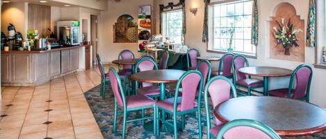 A dining area with round tables and chairs, a kitchen area with appliances, and a clock on the wall.