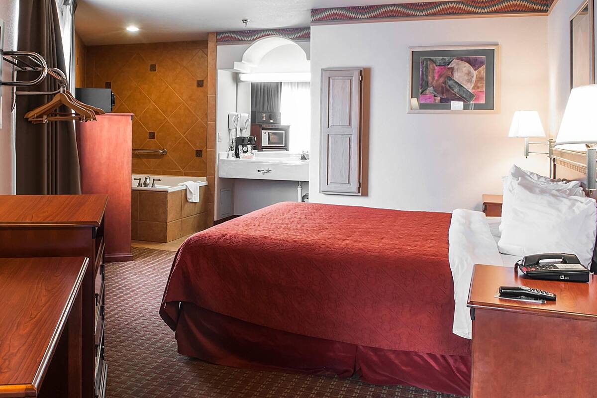 Ein Hotelzimmer mit einem großen Bett, einem Schreibtisch, einer Kommode, einem Schminktisch mit Spiegel und einem Bild an der Wand.