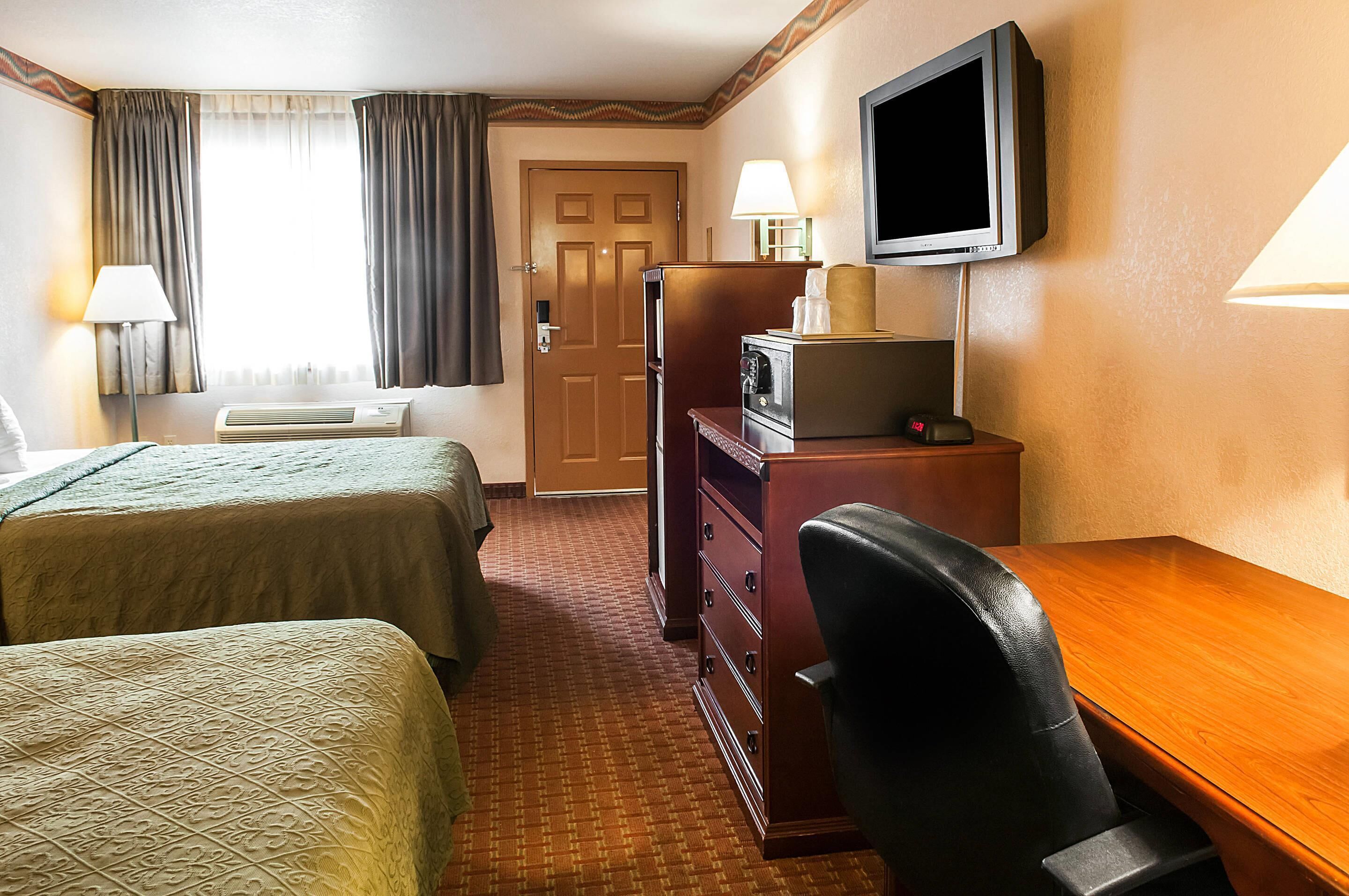 Ein Hotelzimmer mit zwei Betten, einem Schreibtisch, einem Fernseher und einer Tür.