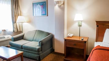 Ein Hotelzimmer mit einer Couch, einem Nachttisch mit Lampe, einem Nachttischtelefon und einem Bett mit roter Decke.