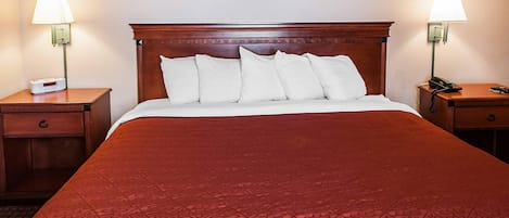 Hotellihuone, jossa on suuri sänky, kaksi yöpöytää lamppuineen, herätyskello ja seinällä oleva kehystetty kuva.