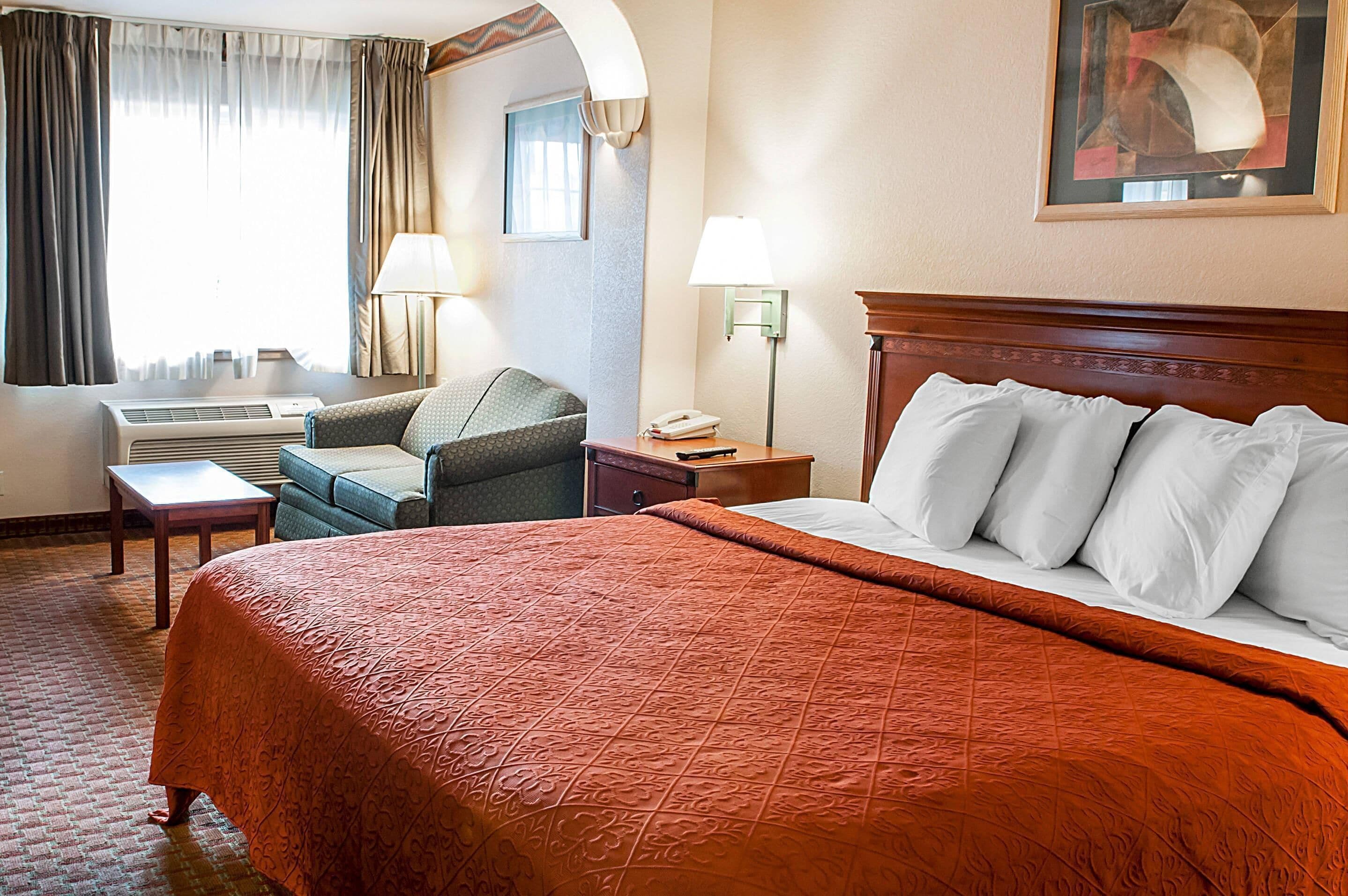A hotel room with a large bed, a desk, a chair, and a window with curtains.