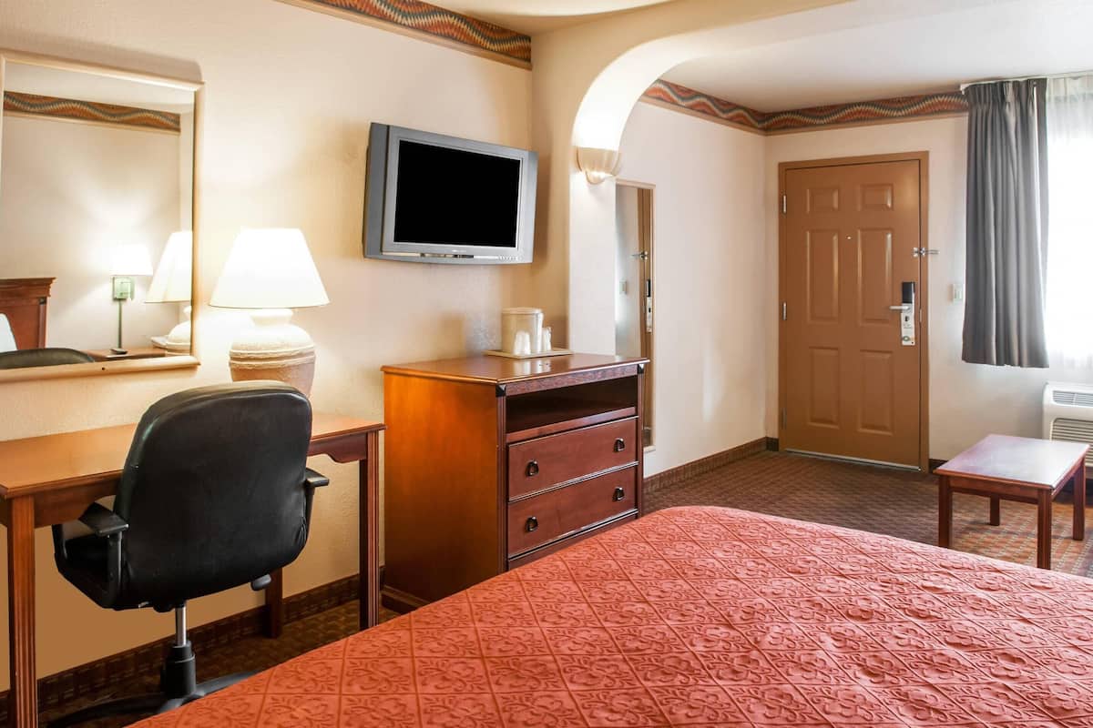 Ein Hotelzimmer mit Bett, Schreibtisch, Stuhl, Fernseher und einer Tür.
