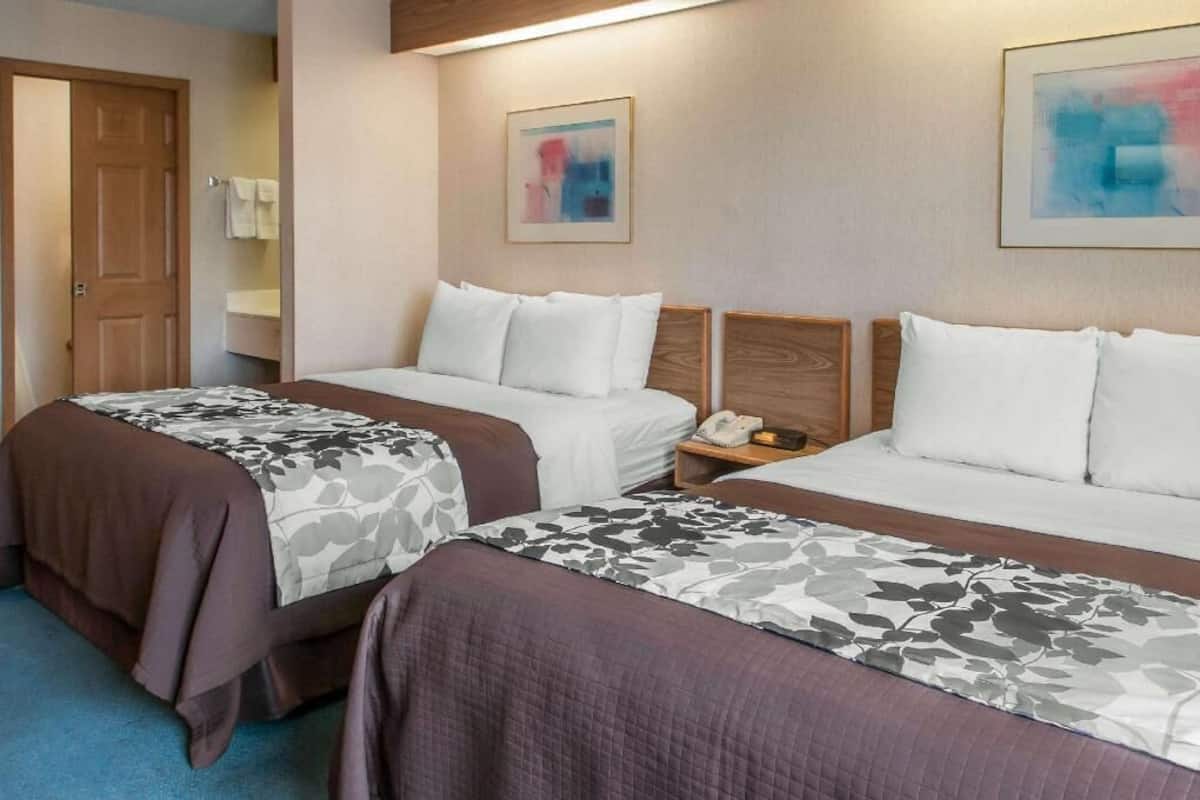 A hotel room with two beds, a wooden headboard, a bedside table with a phone, and a framed abstract painting on the wall.