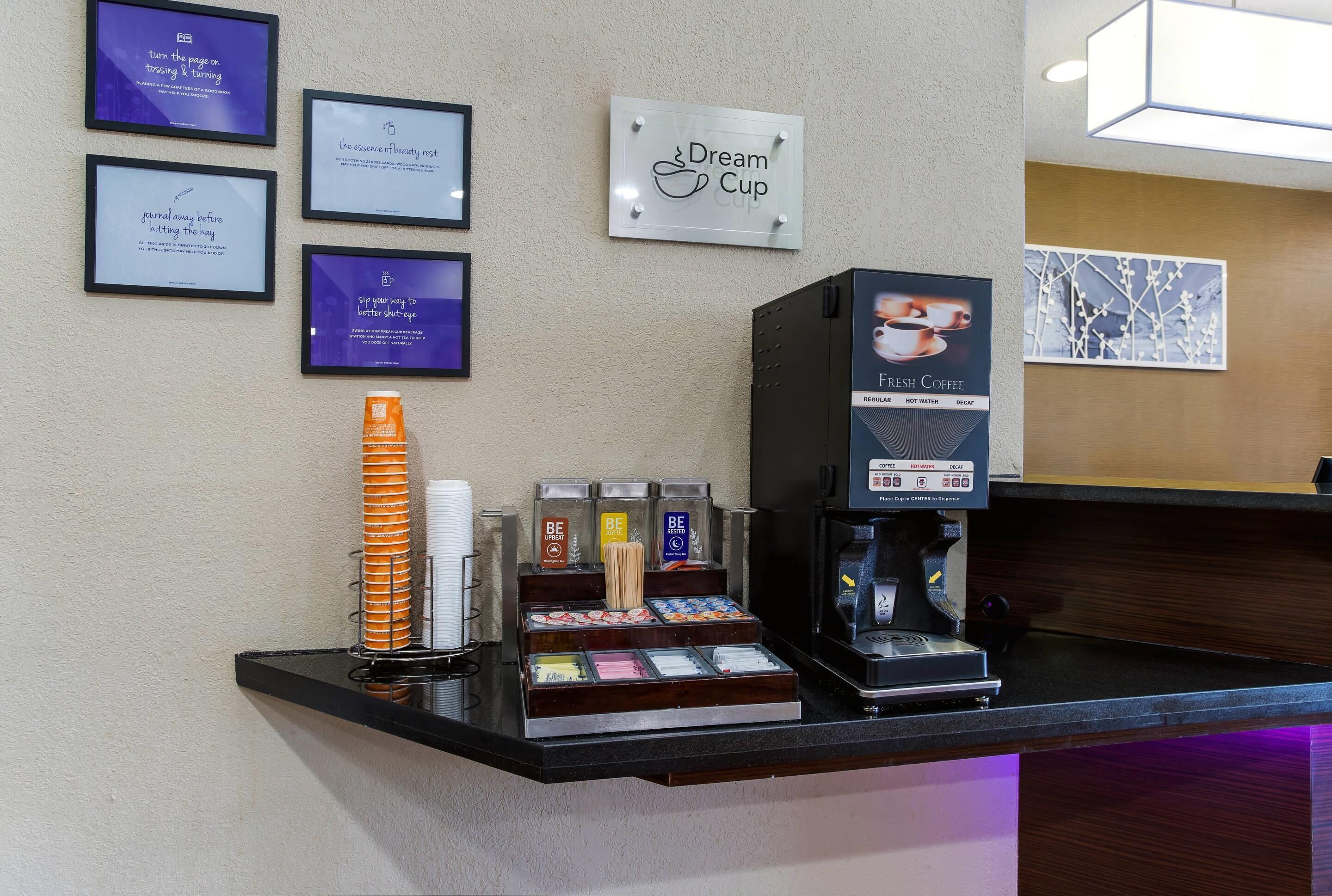 Angolo caffè con macchina da caffè, tazze e un cartello con scritto 'Dream Cup'.