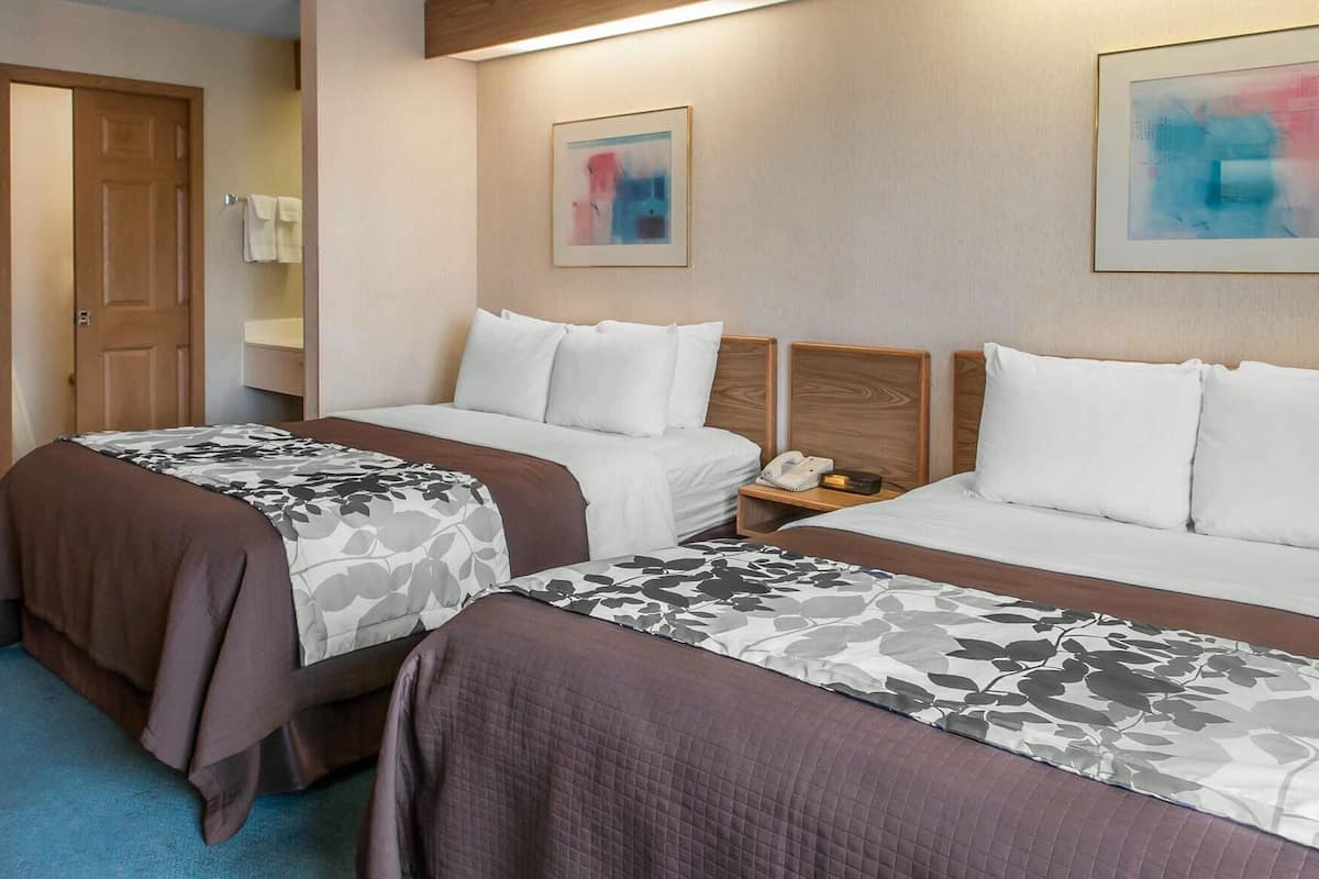 A hotel room with two beds, a wooden door, a nightstand with a phone, and abstract art on the walls.