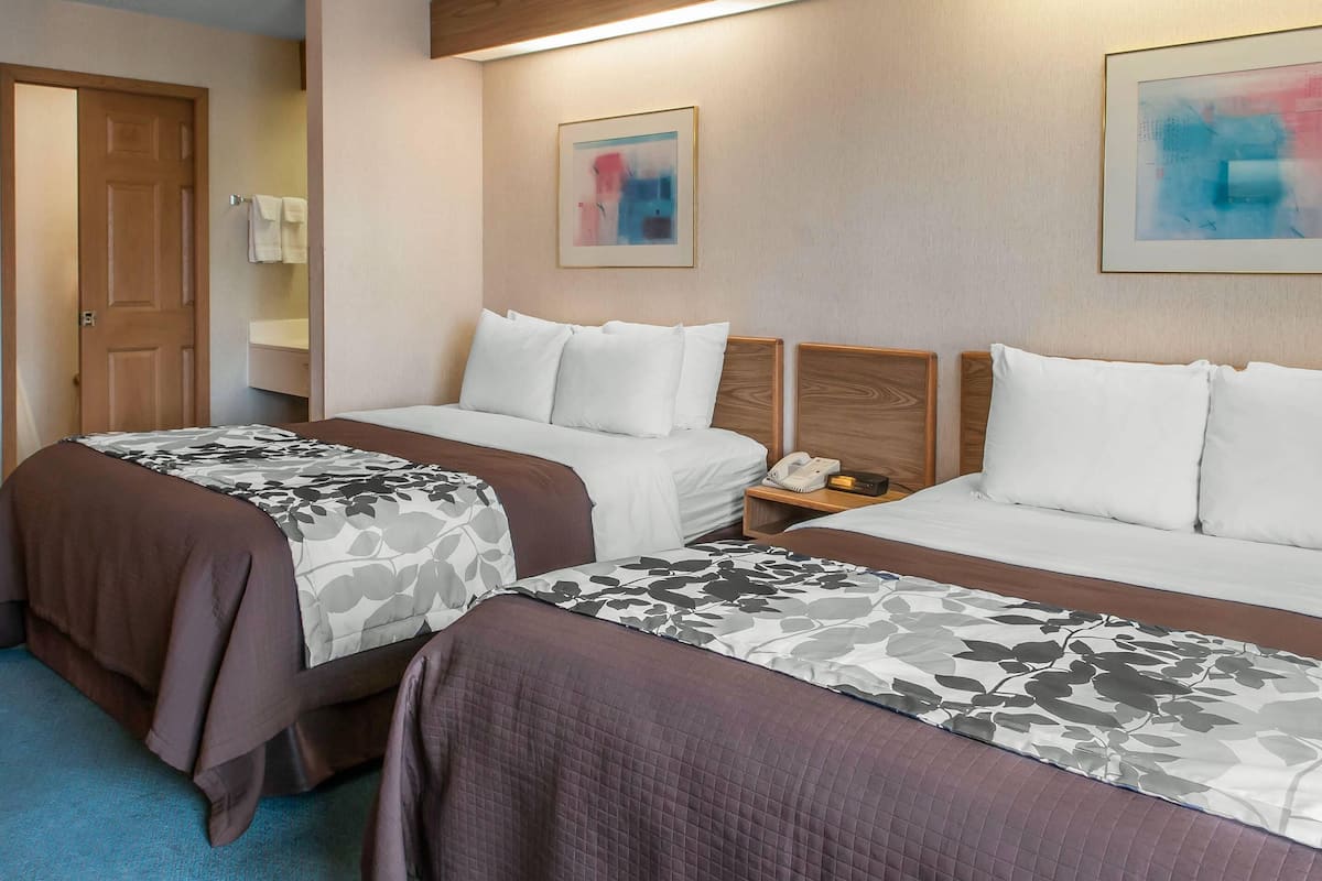 A hotel room with two beds, a wooden headboard, a bedside table with a phone, and a framed abstract painting on the wall.