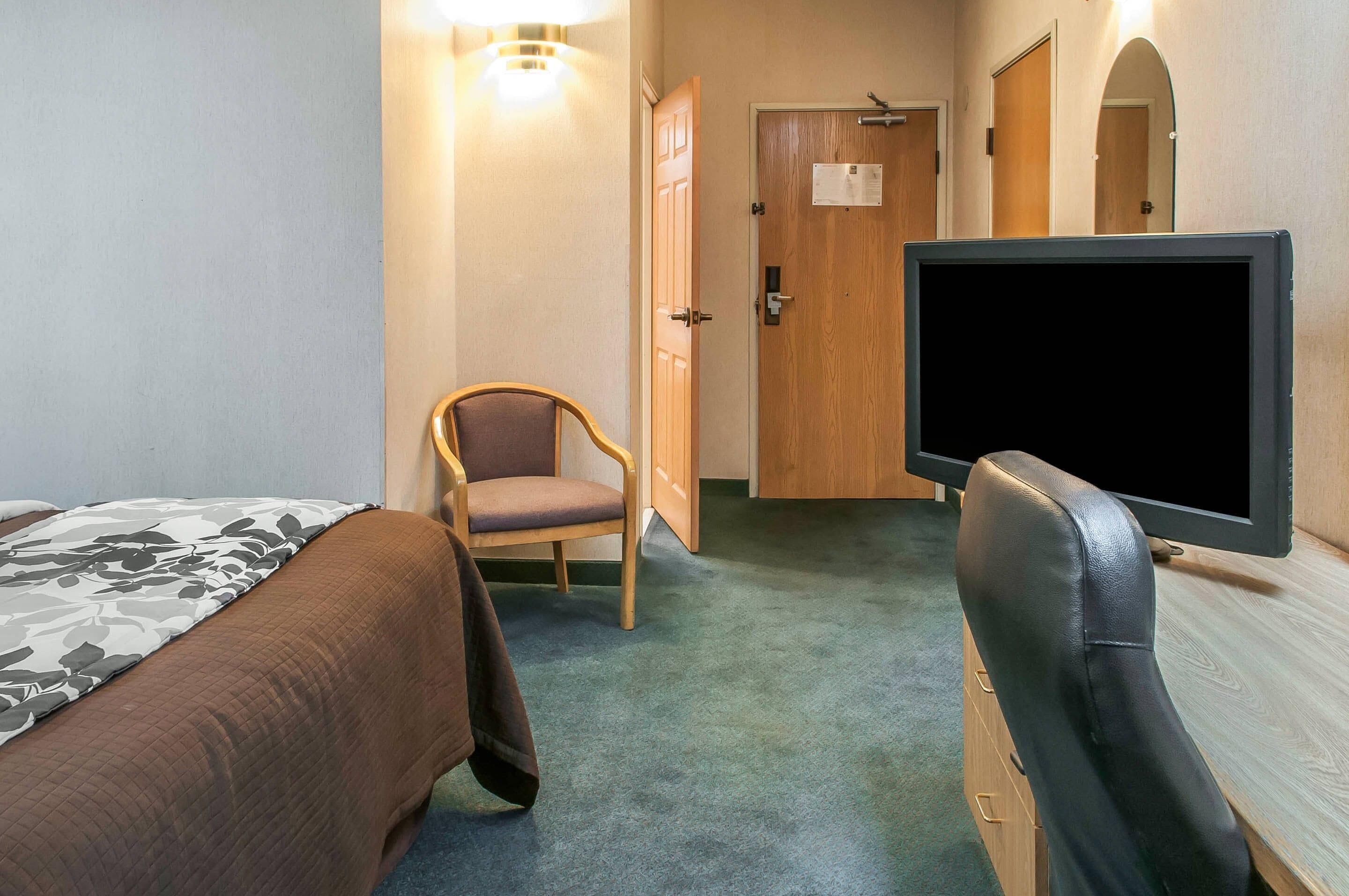 Una habitación de hotel con cama, una silla, escritorio y monitor de computadora.