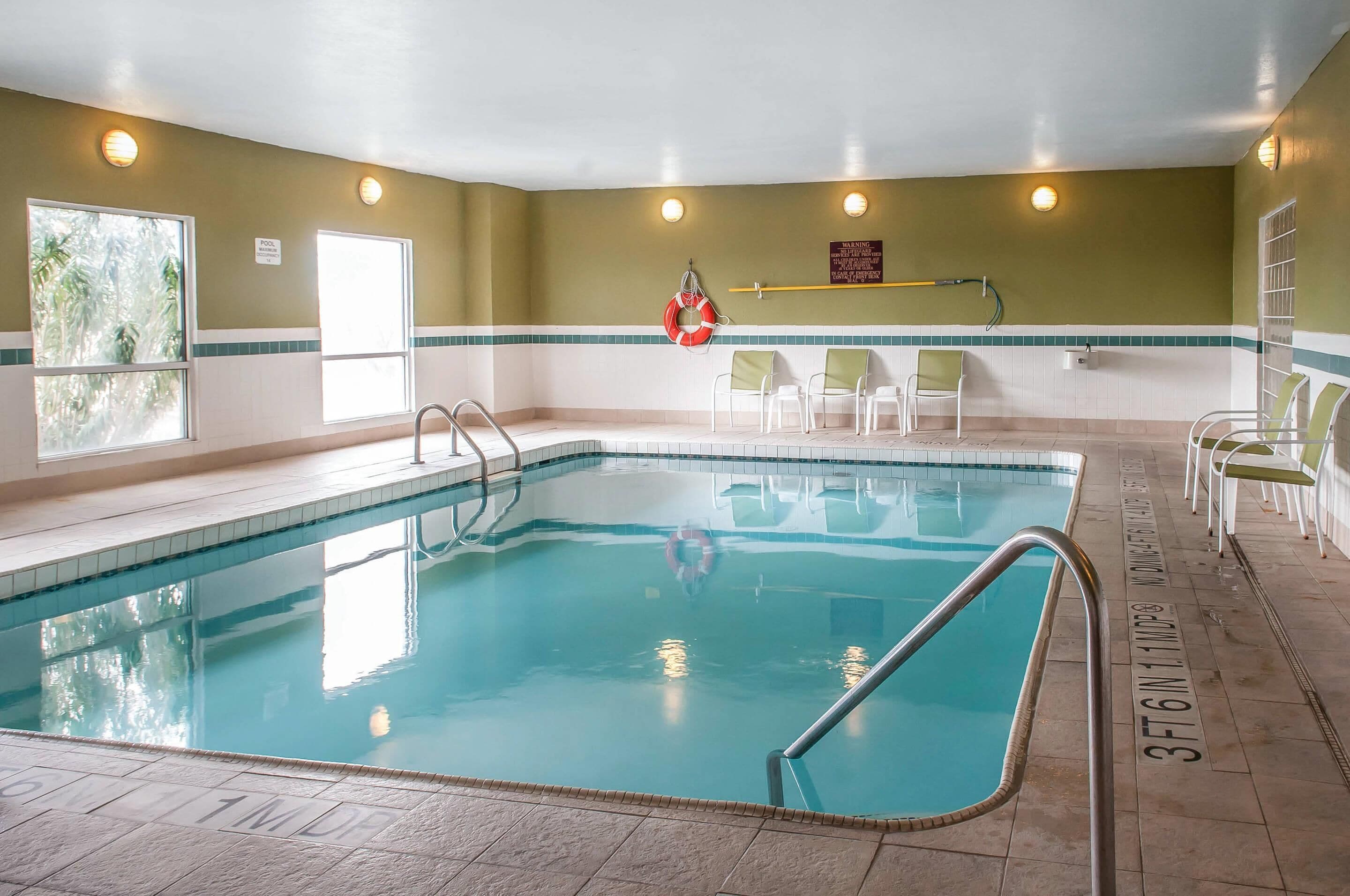 Una piscina interior con agua cristalina, un flotador salvavidas y sillas a lo largo de la piscina.