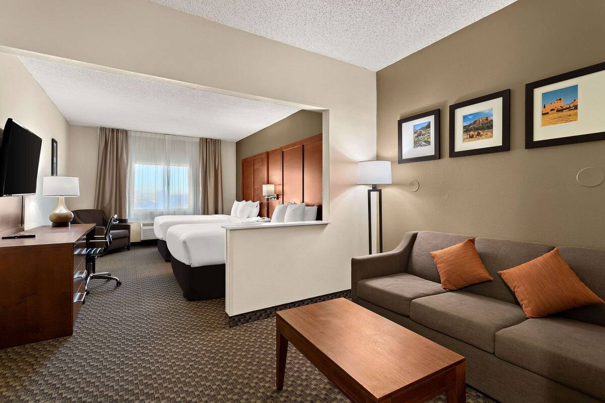 A hotel room with a bed, a sofa, a desk, and a TV. There are framed pictures on the wall.