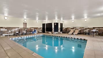 An indoor swimming pool with clear water, surrounded by lounge chairs and a tiled floor.