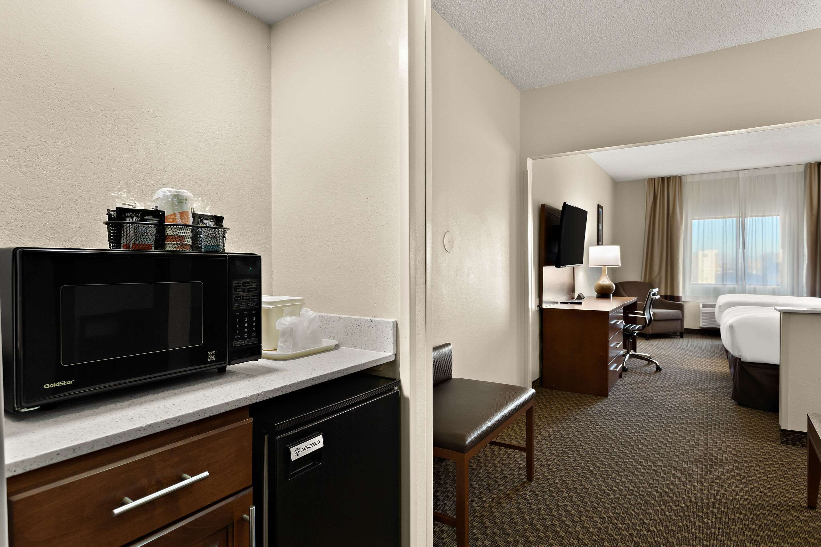 Una habitación de hotel con kitchenette, escritorio, silla, cama y televisión.