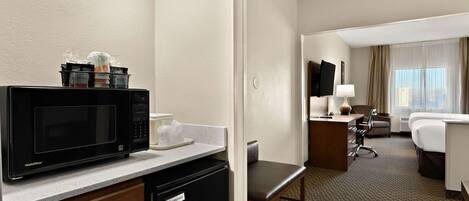Una habitación de hotel con kitchenette, escritorio, silla, cama y televisión.