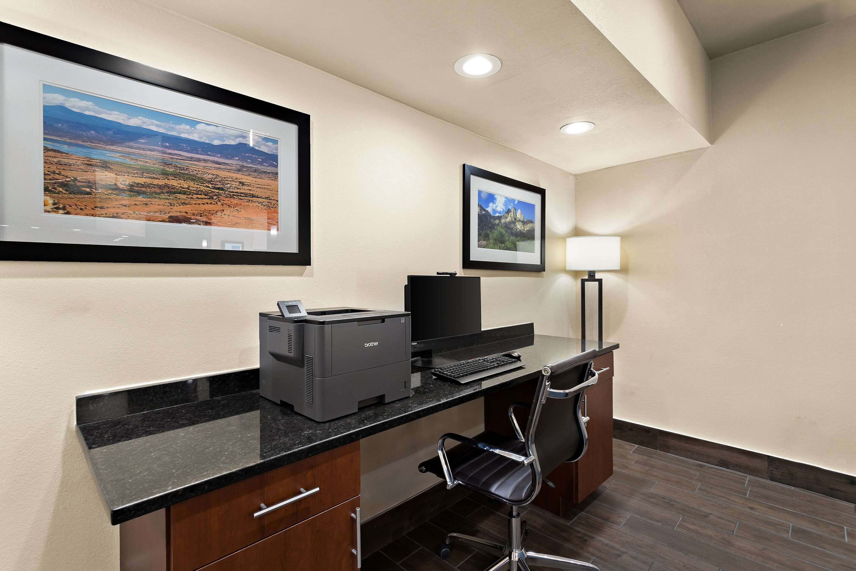 A hotel office with a desktop computer, printer, and framed pictures on the wall.