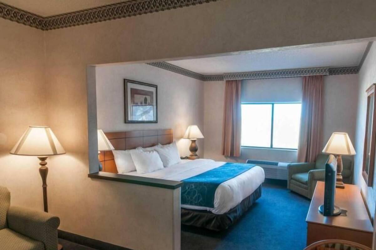 A hotel room with a bed, two bedside lamps, a chair, a desk, and a window with curtains.