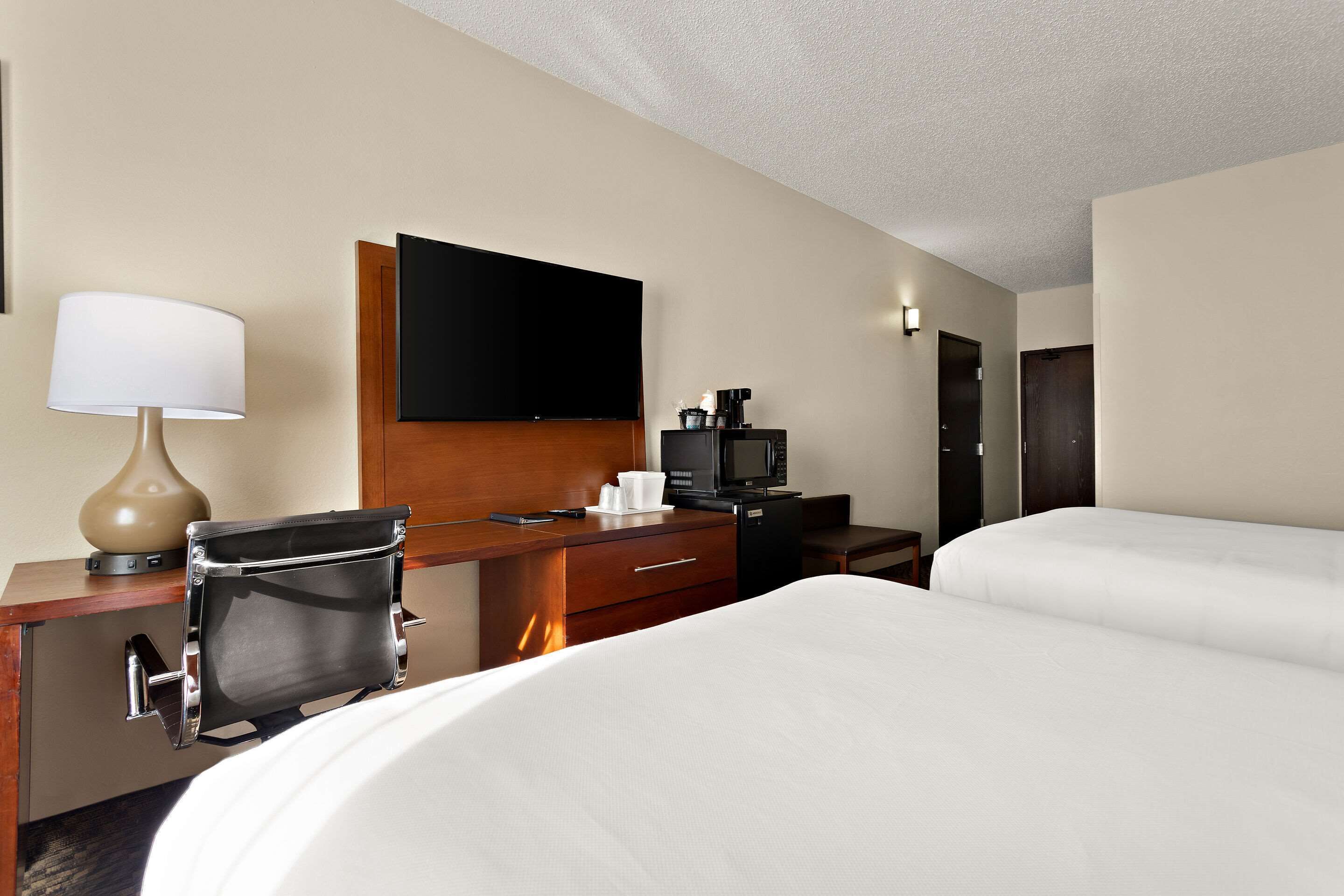 A hotel room with a bed, a desk with a lamp, a flat-screen TV, a coffee maker, and a microwave.