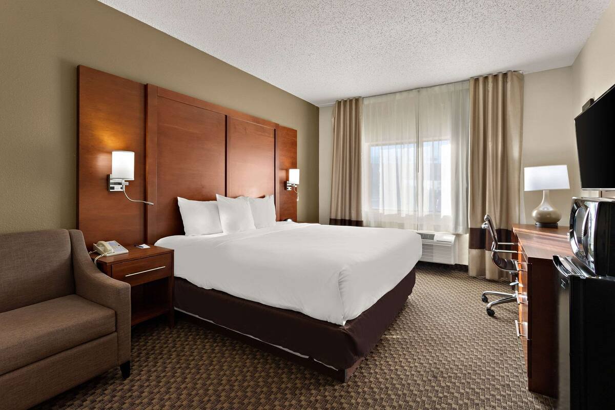 A hotel room with a large bed, a desk with a chair, a TV, and a telephone.