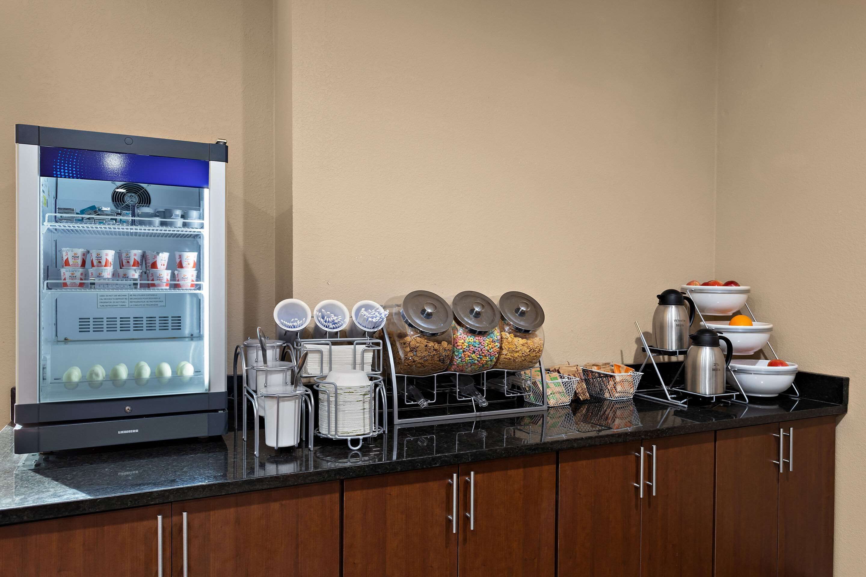 A self-service breakfast bar with a refrigerator, coffee maker, and various food containers.
