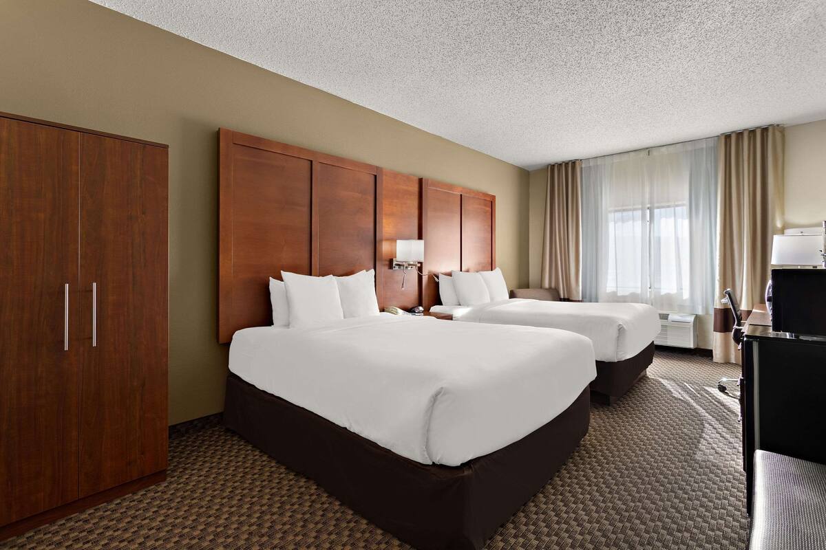 A hotel room with two beds, a wardrobe, a desk, and a TV.