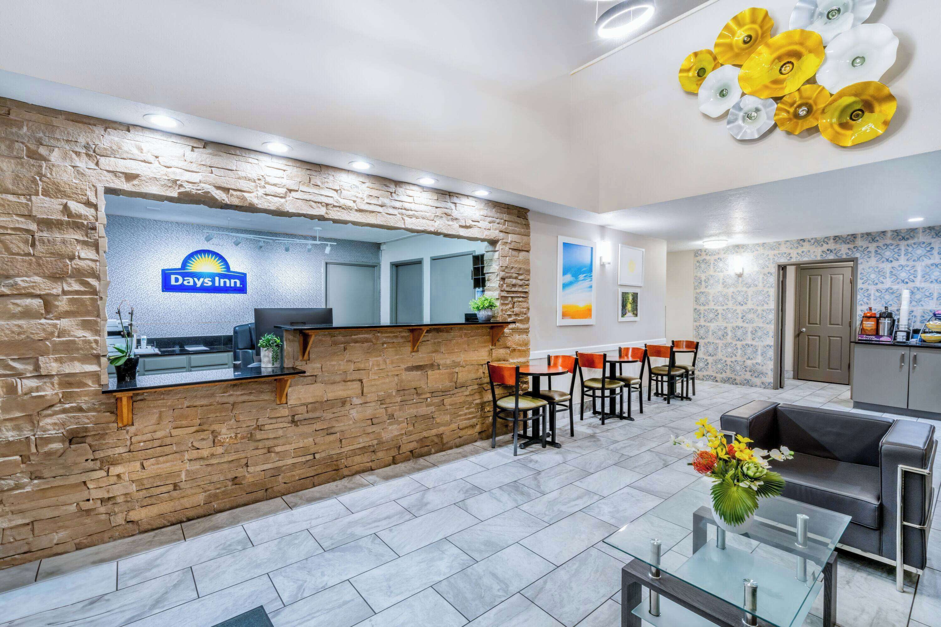 A Days Inn reception area with a stone wall, a reception desk, and a seating area with tables and chairs.