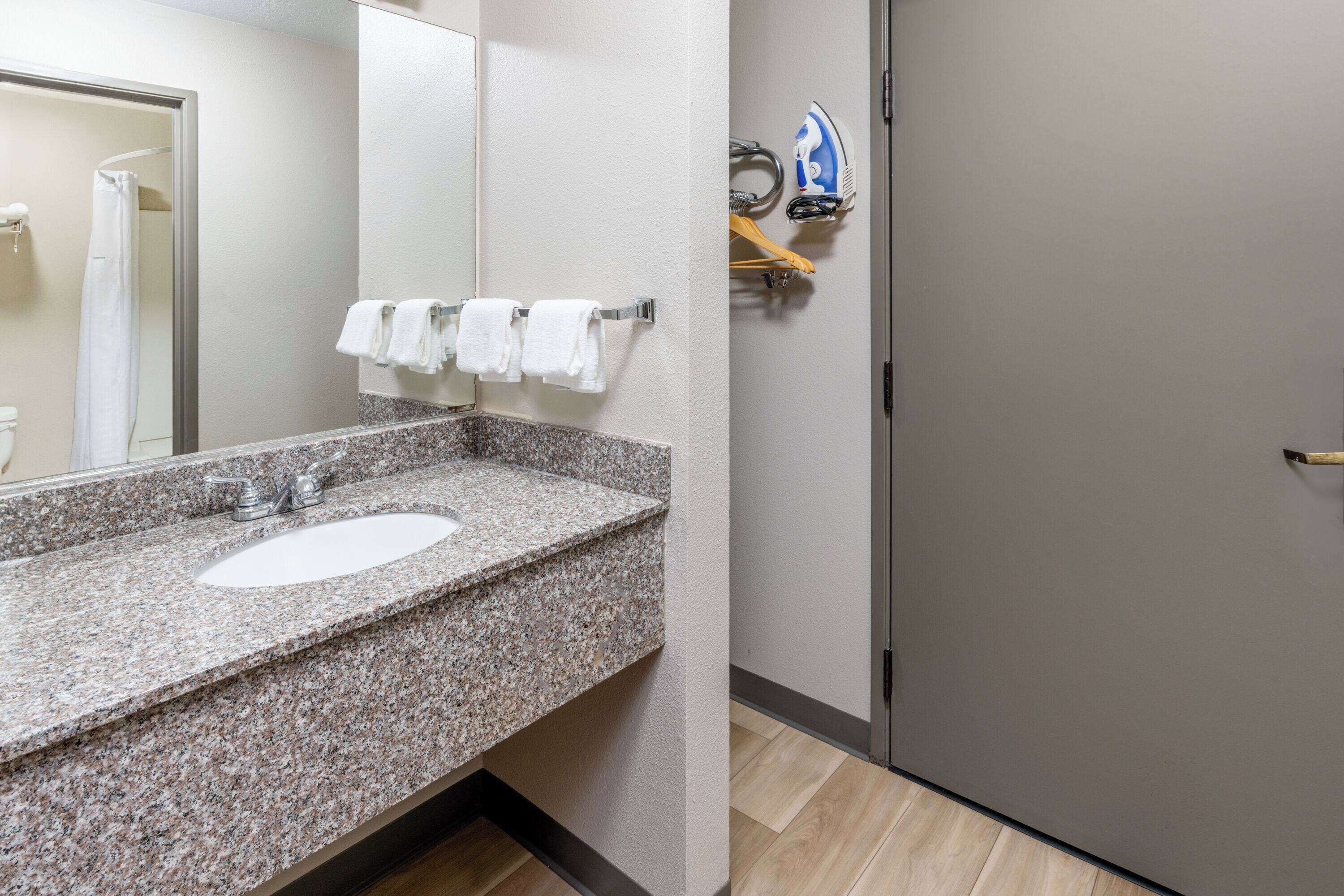 A bathroom with a granite countertop sink, a mirror, and a shower area.