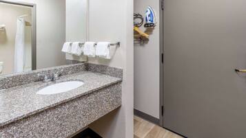A bathroom with a granite countertop sink, a mirror, and a shower area.